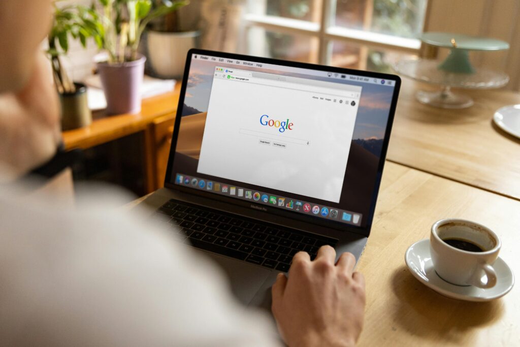 pexels-photo-6961857-6961857-1 An adult using a laptop indoors, browsing Google at a wooden table with coffee.
